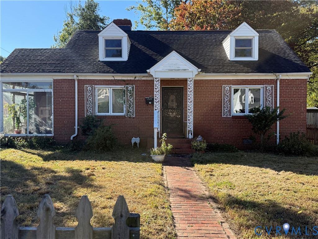 Red brick exterior featuring a shingled roof, two dormer windows, decorative window shutters, and an enclosed side porch