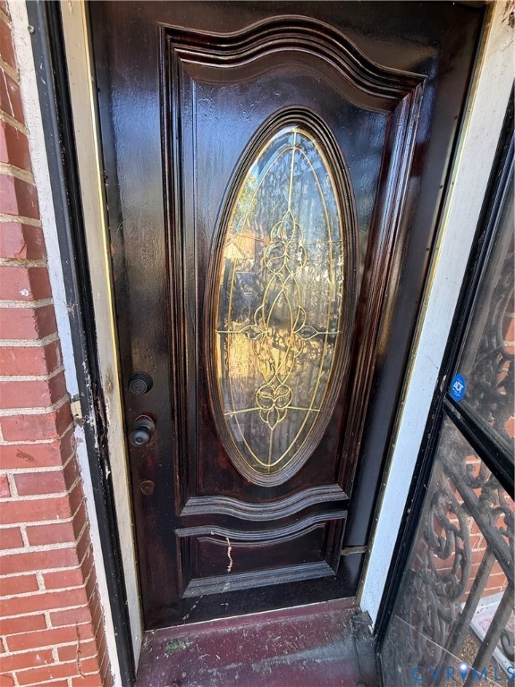 Dark-stained wood entry door featuring an oval glass insert with decorative caming and multi-paneled millwork, flanked by red brick masonry