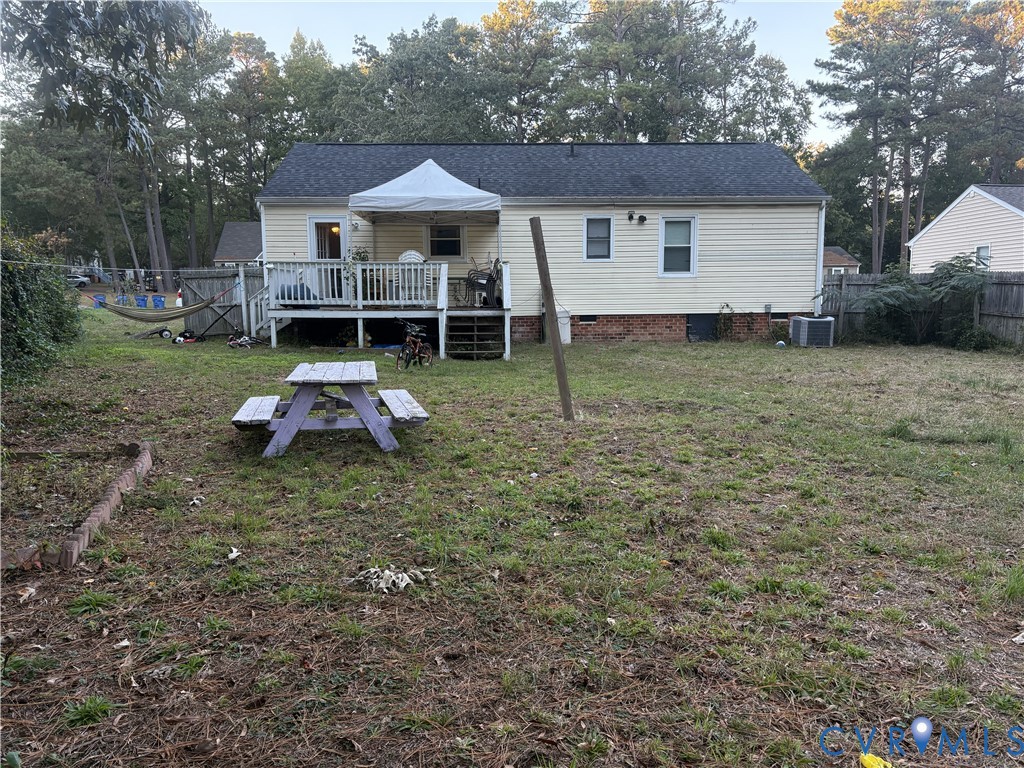 Rear exterior featuring light-colored horizontal siding, a raised wooden deck with railings, and a fenced yard with mature trees