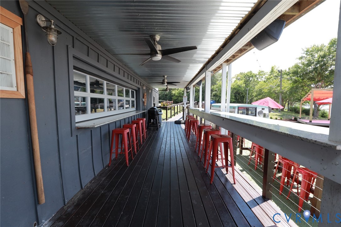 Covered outdoor deck featuring a corrugated metal ceiling, dual ceiling fans, built-in bar service counter, and cable railing