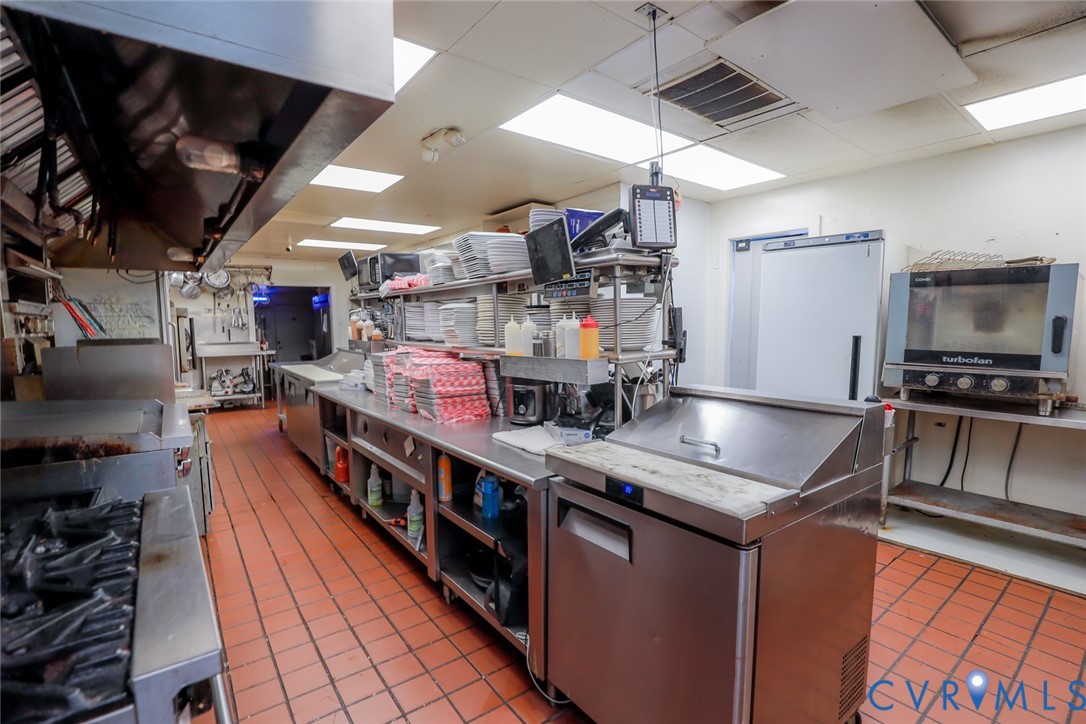 Commercial kitchen featuring stainless steel prep stations, industrial-grade range equipment, a professional exhaust hood system, a dedicated convection oven, and durable tile flooring