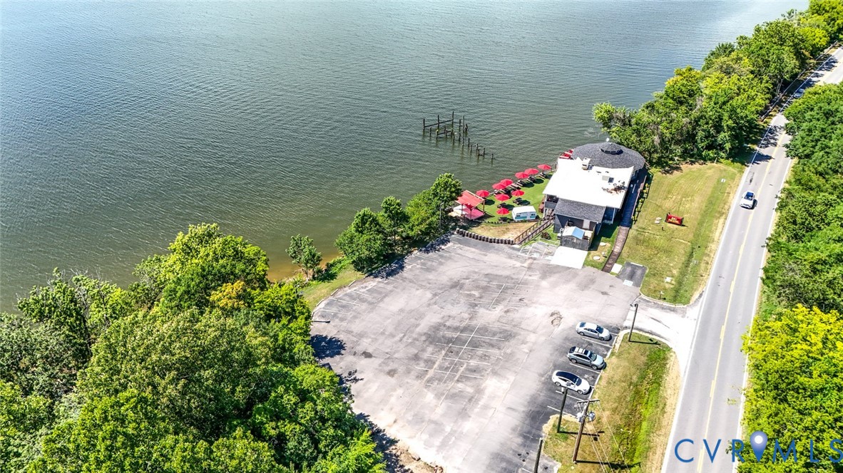Waterfront property featuring a paved parking area, mature trees, and direct access to the shoreline