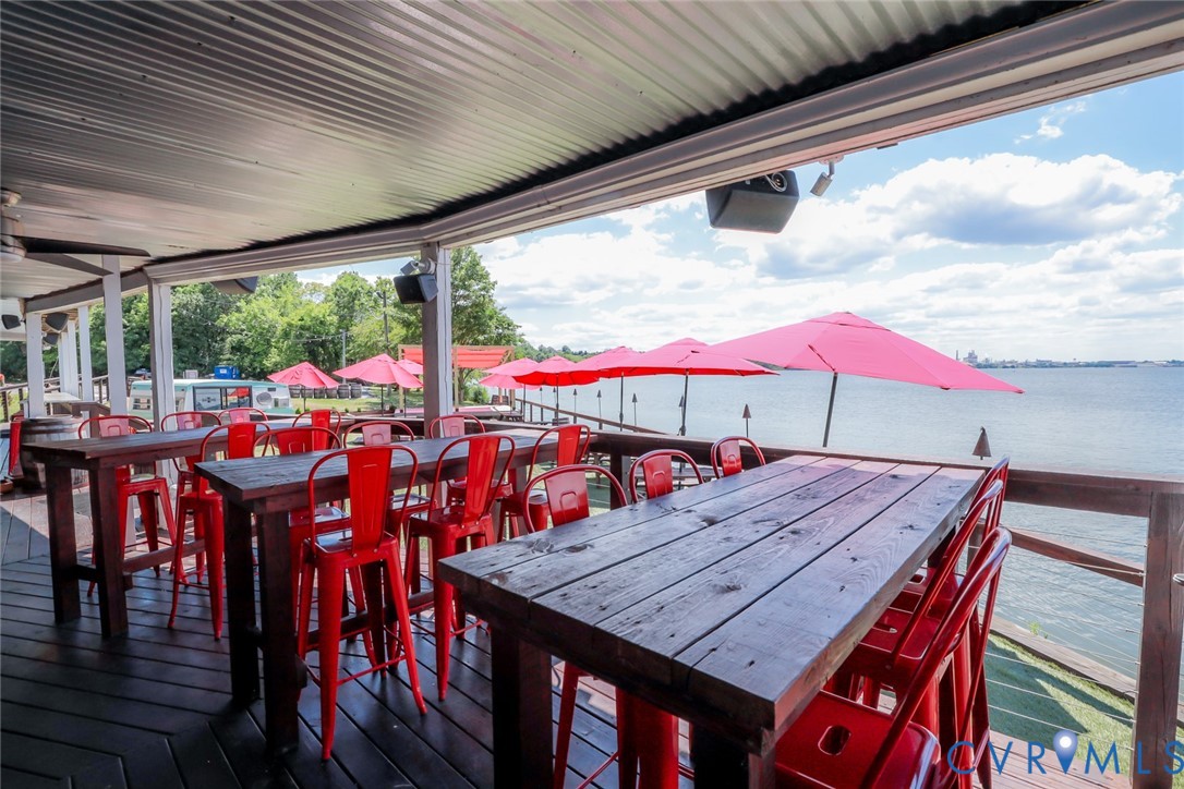 Covered deck with corrugated metal ceiling, wood plank flooring, and wooden railings overlooking a body of water