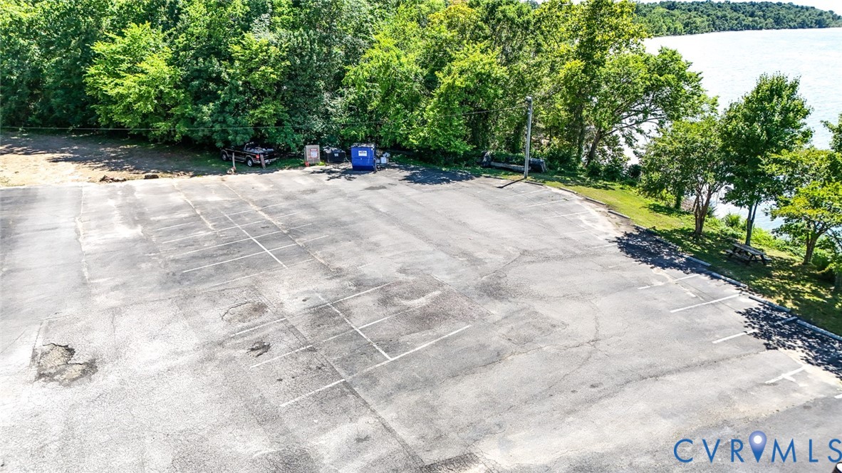 Asphalt-paved parking area featuring marked spaces, perimeter mature trees, and waterfront proximity