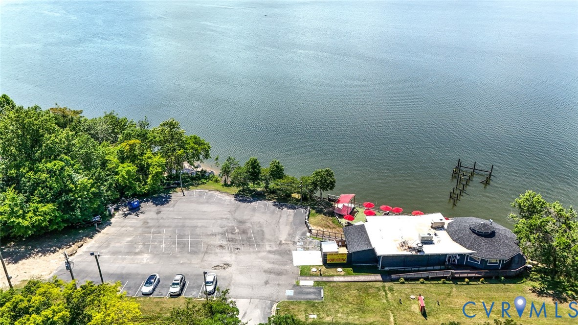 Waterfront property featuring an expansive asphalt parking lot, private pier pilings, and mature perimeter trees