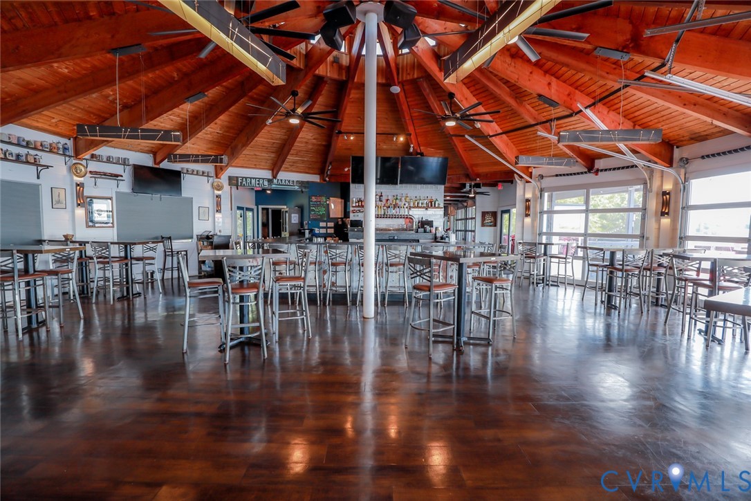 Expansive open-concept space featuring a vaulted, radial timber-truss ceiling, stained concrete flooring, multi-panel glass garage-style doors, and a built-in central bar