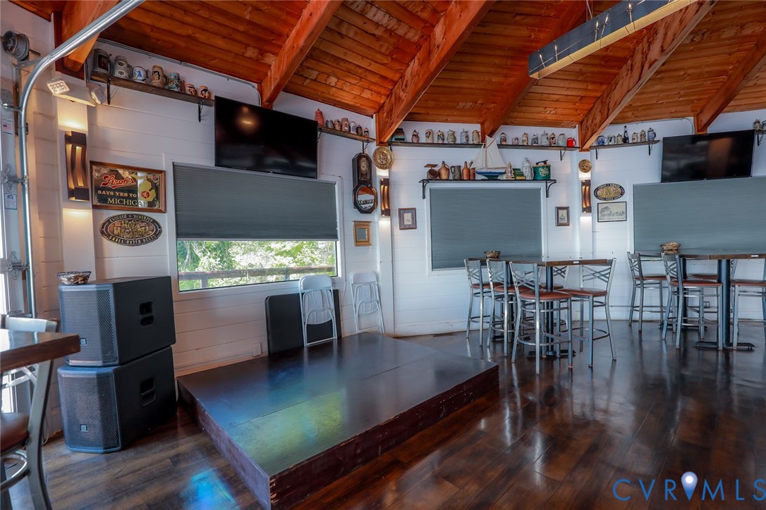 Vaulted ceiling with exposed wood beams, wood-finish flooring, white horizontal wall paneling, and built-in wall shelving