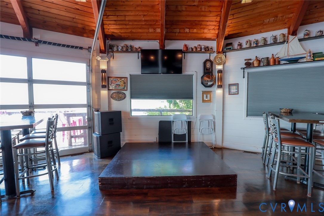 Exposed wood-beam vaulted ceiling with tongue-and-groove planking, polished wood-finish flooring, glass-paned roll-up garage door, raised wood platform, and built-in wall-mounted shelving