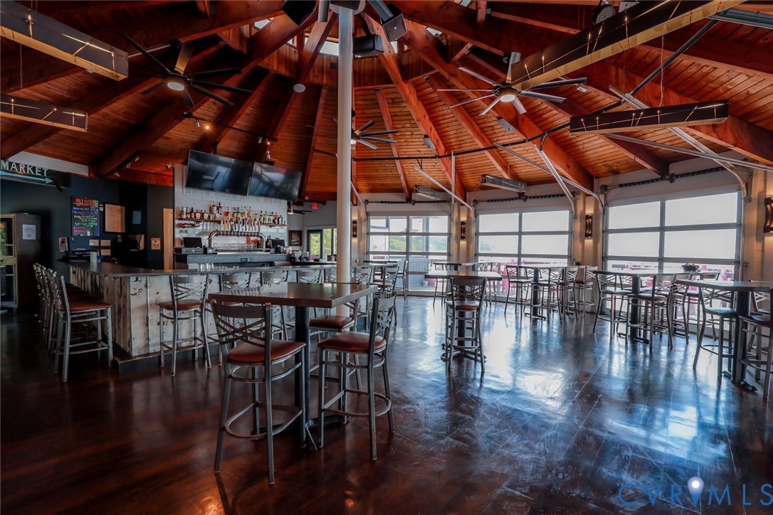 Expansive interior featuring an exposed wood-beam conical ceiling, polished wood-finish flooring, a built-in bar with light-toned wood paneling, and multiple glass-paned garage-style doors