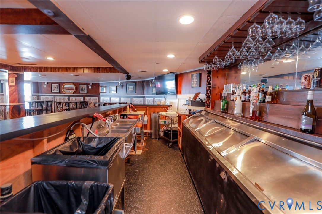 Custom wooden bar area featuring a built-in multi-basin stainless steel sink, glass stemware rack, mirrored backsplash, and recessed lighting