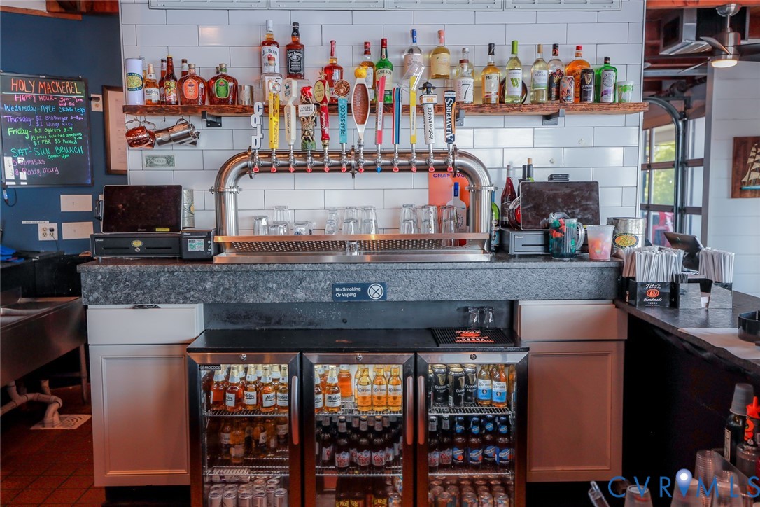 Custom bar station featuring a professional multi-tap draft system, white subway tile backsplash, stone-surface countertop, built-in triple-door glass refrigeration, and floating wood shelving