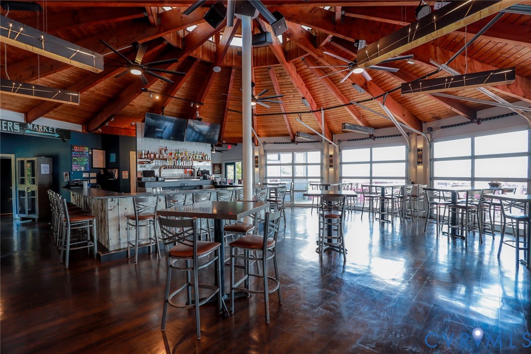 Vaulted wood-paneled ceiling with exposed beams, polished wood-finish flooring, full-length roll-up glass garage doors, and integrated bar counter with built-in draft system