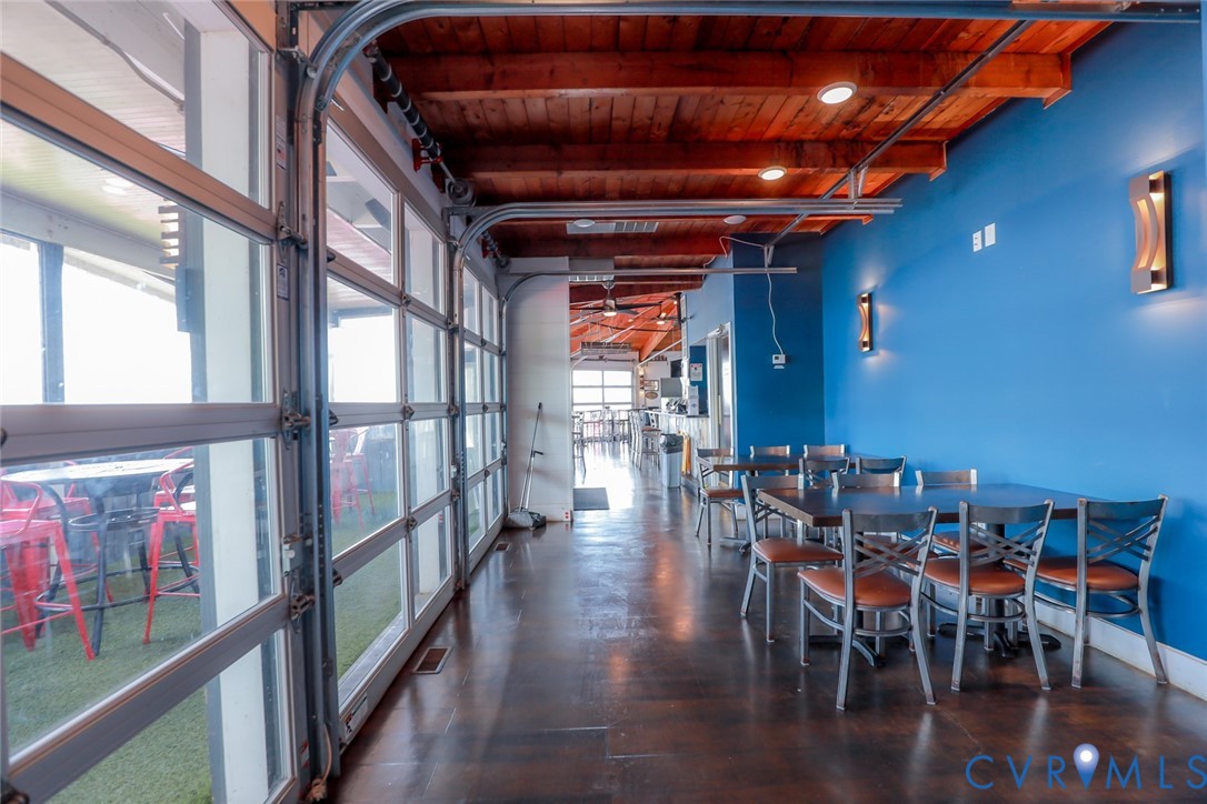Industrial-style space featuring retractable glass garage-style doors, exposed wood-beam ceilings, polished dark flooring, and wall-mounted sconce lighting
