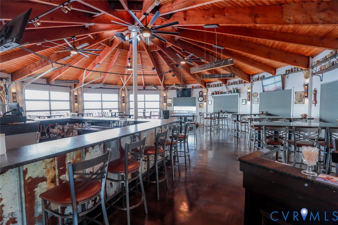 Expansive vaulted ceiling with exposed natural wood rafters, built-in wrap-around bar with integrated counter, dark polished concrete flooring, and multi-pane window wall