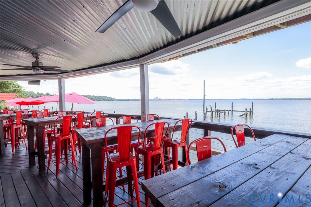 Covered waterfront deck featuring corrugated metal roofing, ceiling fans, wood-plank decking, and perimeter railing