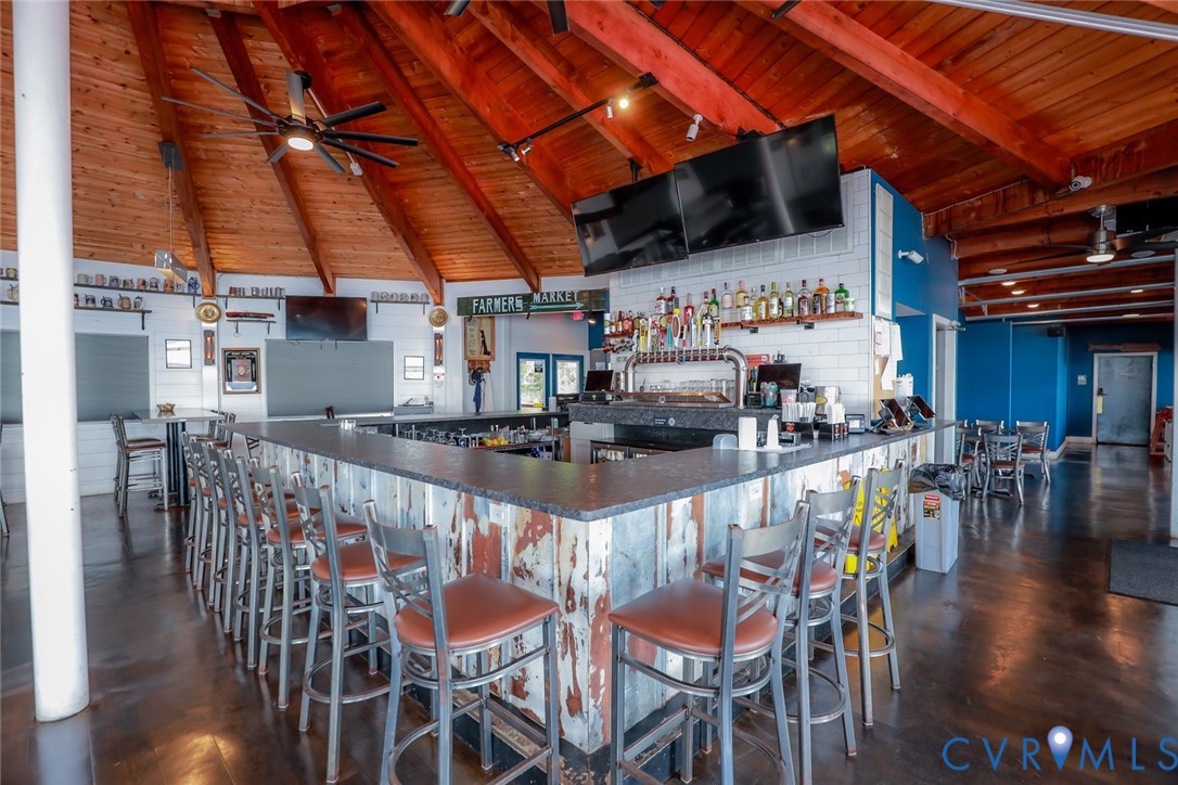 Bar area featuring a vaulted wood-plank ceiling with exposed beams, a multi-tiered stone-topped bar, corrugated metal paneling, white subway tile backsplash, and polished concrete flooring