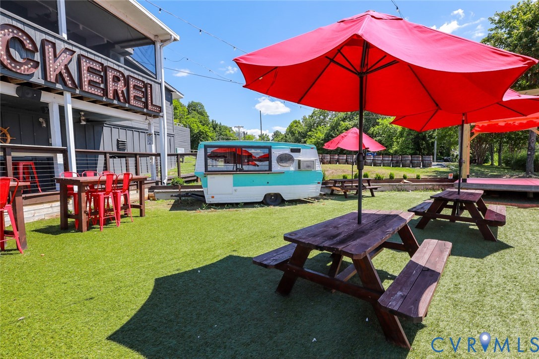 Outdoor recreational space featuring synthetic turf, overhead string lighting, and wood-surface picnic tables