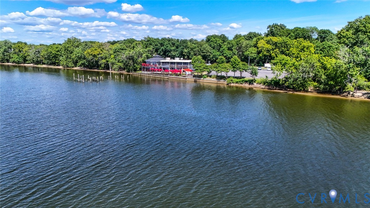 Waterfront property featuring a multi-level structure, paved parking area, wooden dock pilings, and expansive natural shoreline