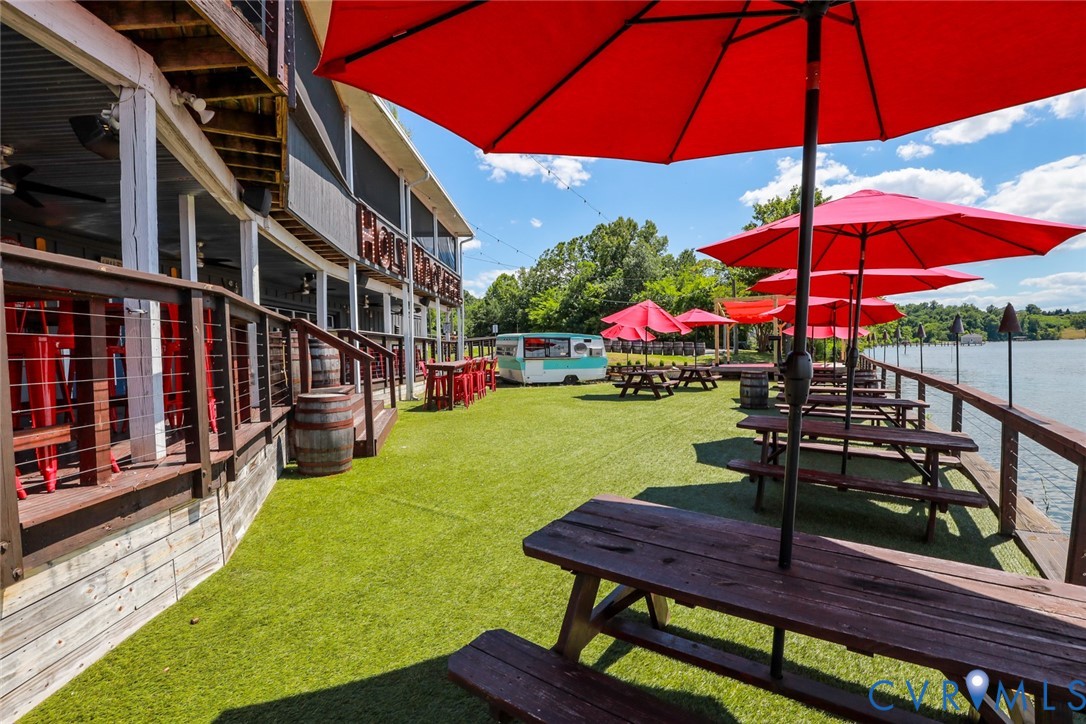 Waterfront outdoor space featuring a tiered wood deck, synthetic turf surface, metal cable railings, and multi-level structural support beams