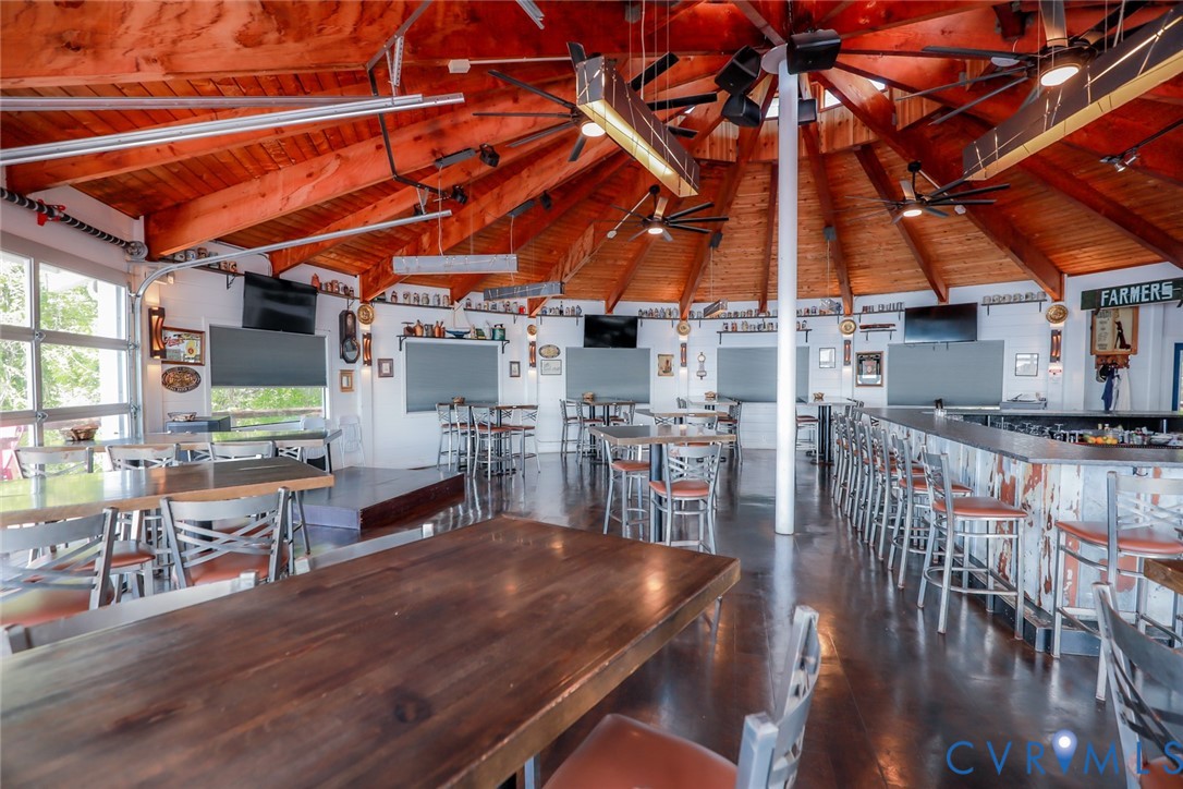 Circular rotunda space featuring vaulted exposed wood-beam ceilings, multiple ceiling fans, integrated bar area with built-in counter, and glass garage-style doors
