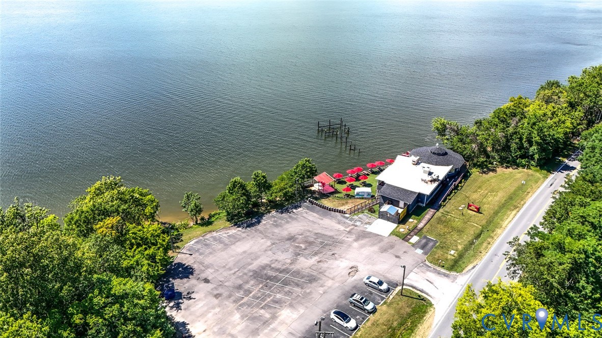 Waterfront property featuring direct access to the shore, an expansive paved parking area, and mature perimeter trees