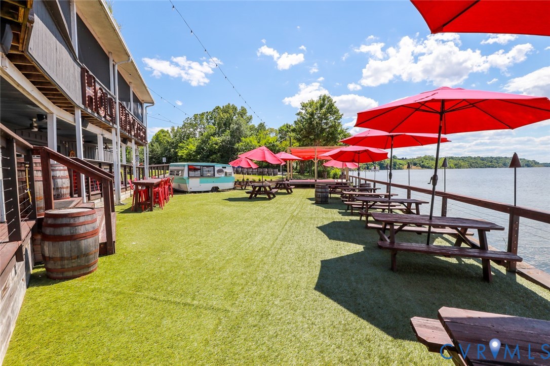 Extensive waterfront patio featuring synthetic turf, overhead string lighting, a wooden perimeter railing, and a multi-level deck structure