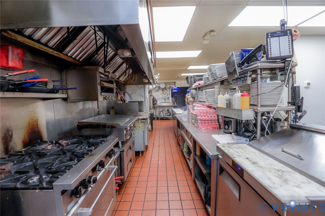 Commercial kitchen featuring a stainless steel range, heavy-duty ventilation hood, stainless steel work surfaces, and tiled flooring