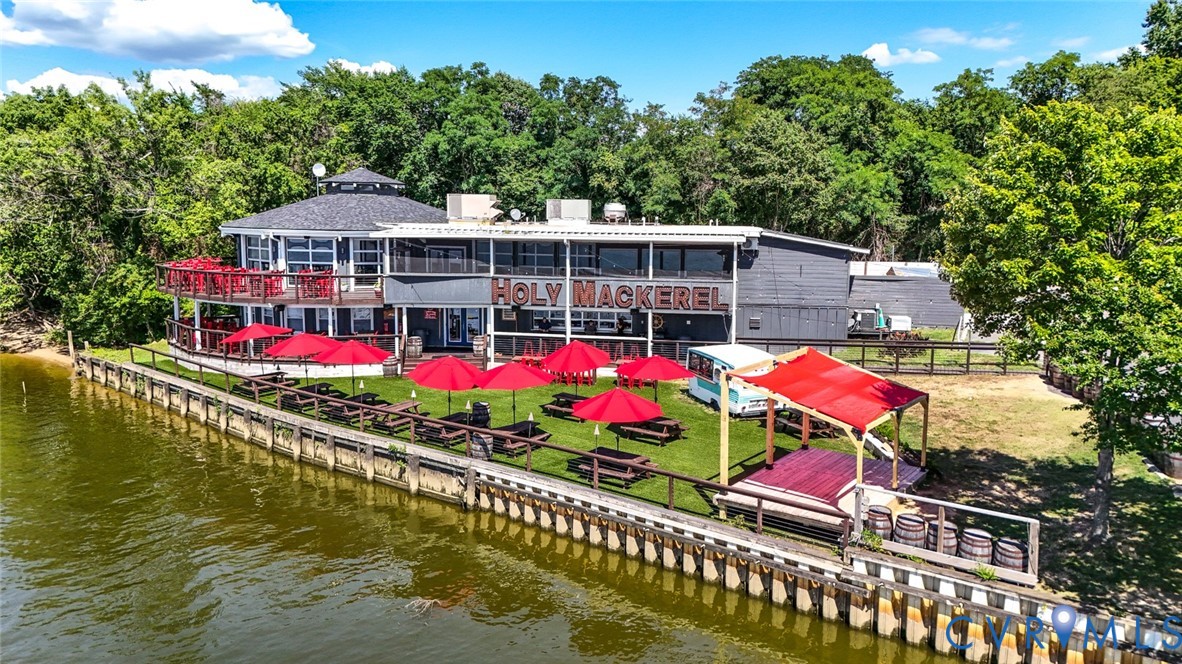 Waterfront commercial property featuring direct bulkhead access, a multi-level deck, expansive lawn, and mature perimeter trees