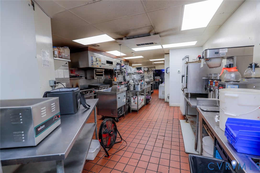 Commercial kitchen space featuring stainless steel work surfaces, a stainless steel exhaust hood, tile flooring, and integrated recessed lighting