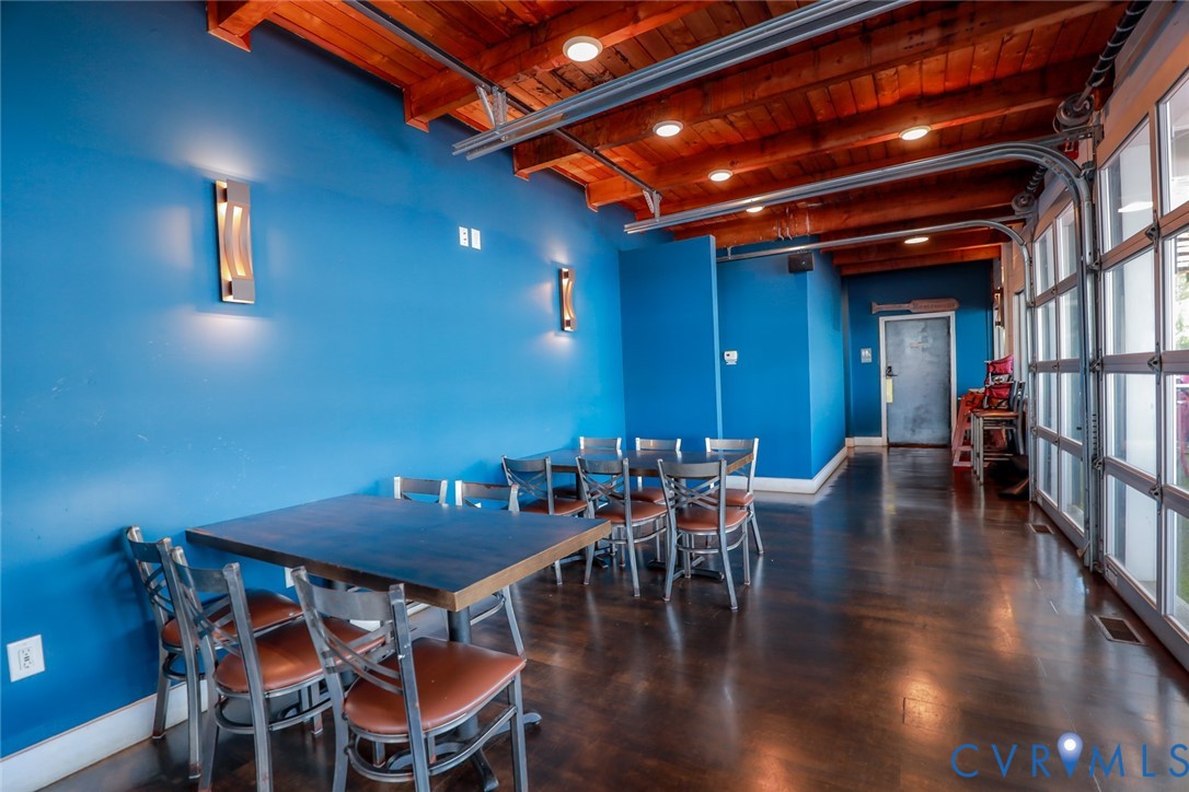 Exposed wood-beam ceiling with recessed lighting, stained concrete flooring, full-wall glass garage door, and modern wall-mounted sconces