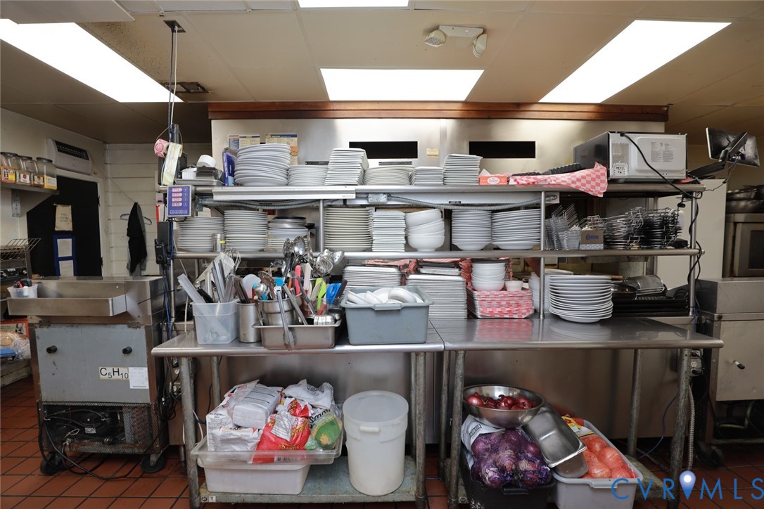 Commercial kitchen workspace featuring stainless steel preparation counters, integrated shelving units, and ceramic tile flooring