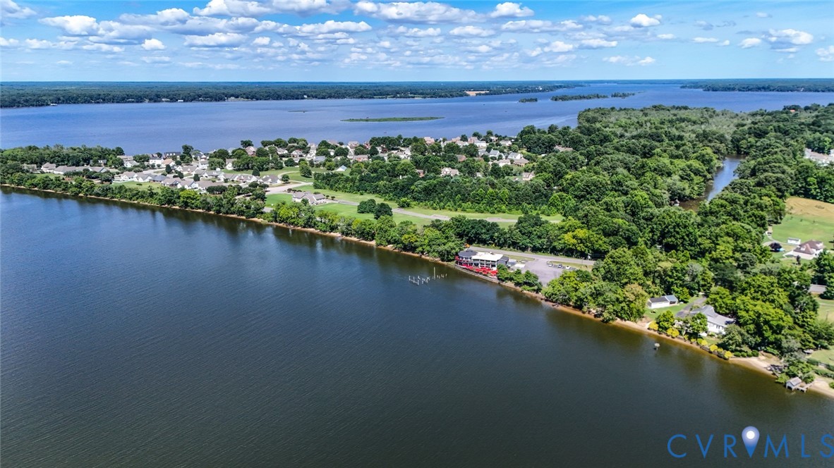 Aerial perspective of waterfront property featuring extensive shoreline, private pier, paved driveway, and mature landscaping