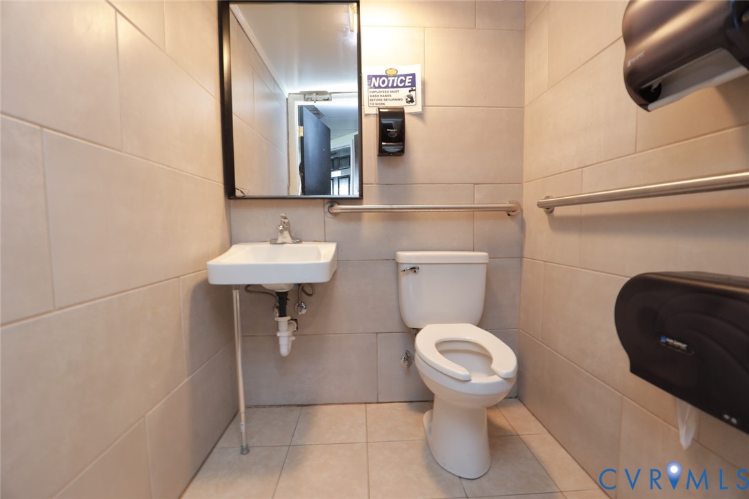 Restroom featuring large-format wall tiling, wall-mounted sink with metal support, mirror with black frame, and installed safety grab bars