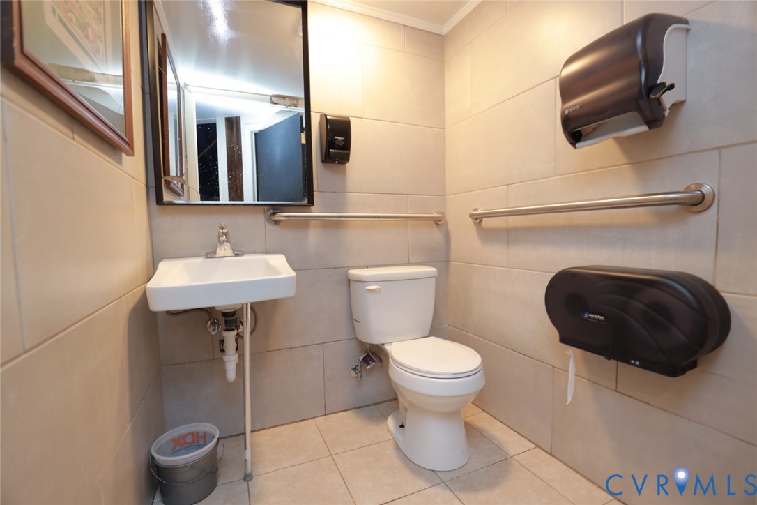 Neutral-toned wall and floor tiling, wall-mounted sink, rectangular vanity mirror, and installed horizontal grab bars