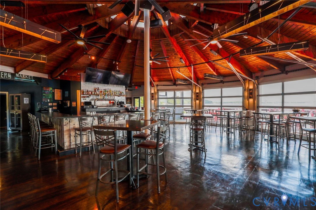 Exposed wood beam vaulted ceiling with a circular design, polished wood flooring, built-in bar, and glass-paneled garage-style wall partitions