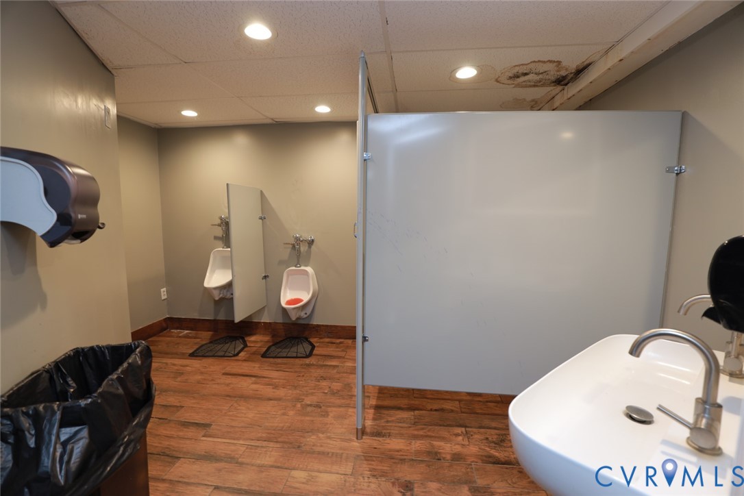 Restroom featuring wood-finish flooring, recessed lighting, wall-mounted urinals with privacy partitions, and a vessel sink with a metal faucet