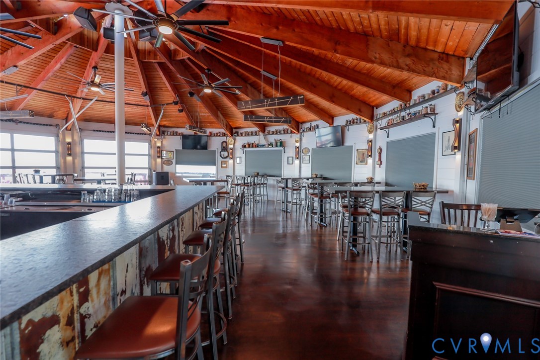 Expansive circular room featuring a vaulted, radial wood-beam ceiling, polished concrete flooring, built-in bar with dark stone-surface countertops, and rustic metal-panel detailing