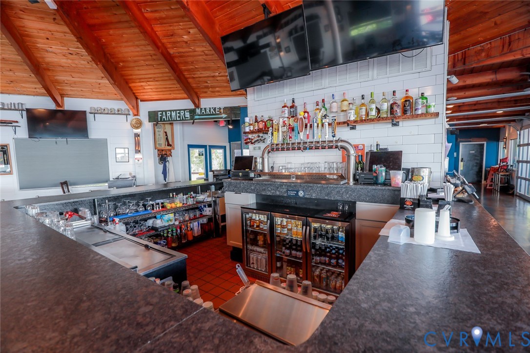 Full-service bar area featuring a wrap-around stone-finish countertop, multi-tap draft system, under-counter refrigeration, tile backsplash, and vaulted wood-paneled ceiling
