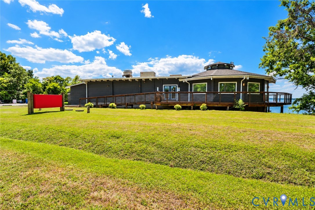 Exterior featuring dark horizontal siding, a rounded roofline, an expansive wraparound deck with railing, and a sloped lawn