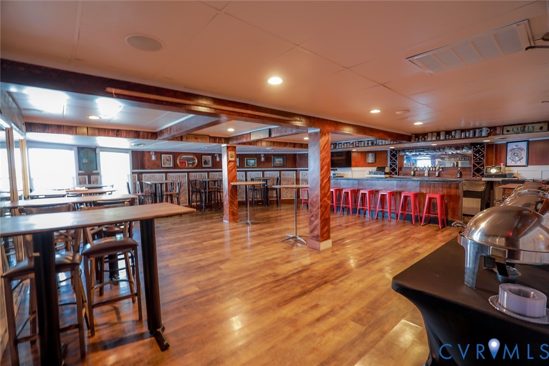 Open-concept space featuring wood-finish flooring, a built-in bar with mirror backing, recessed lighting, and wood-paneled structural columns