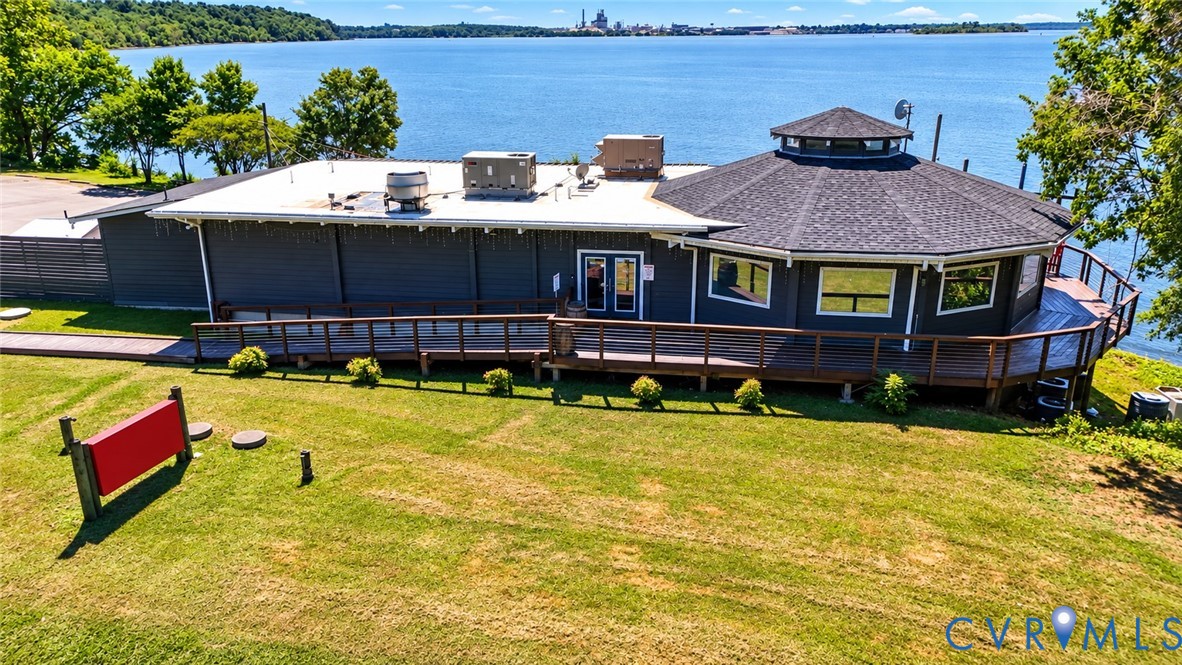 Waterfront property featuring a wraparound wood deck, exterior wood siding, a multi-faceted roofline, and expansive grounds