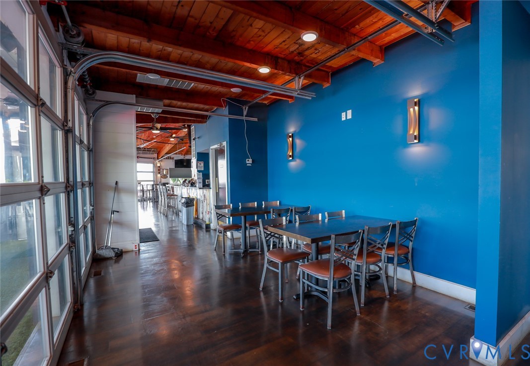 Exposed wood-beam ceiling featuring recessed lighting, dark wood-finish flooring, glass panel overhead garage-style door, and integrated wall sconces