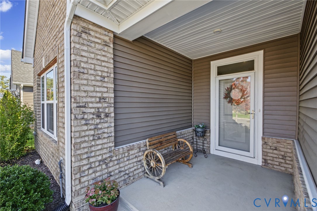 Covered entryway featuring brick detailing  and a glass-paneled entry door with an overhead transom window.