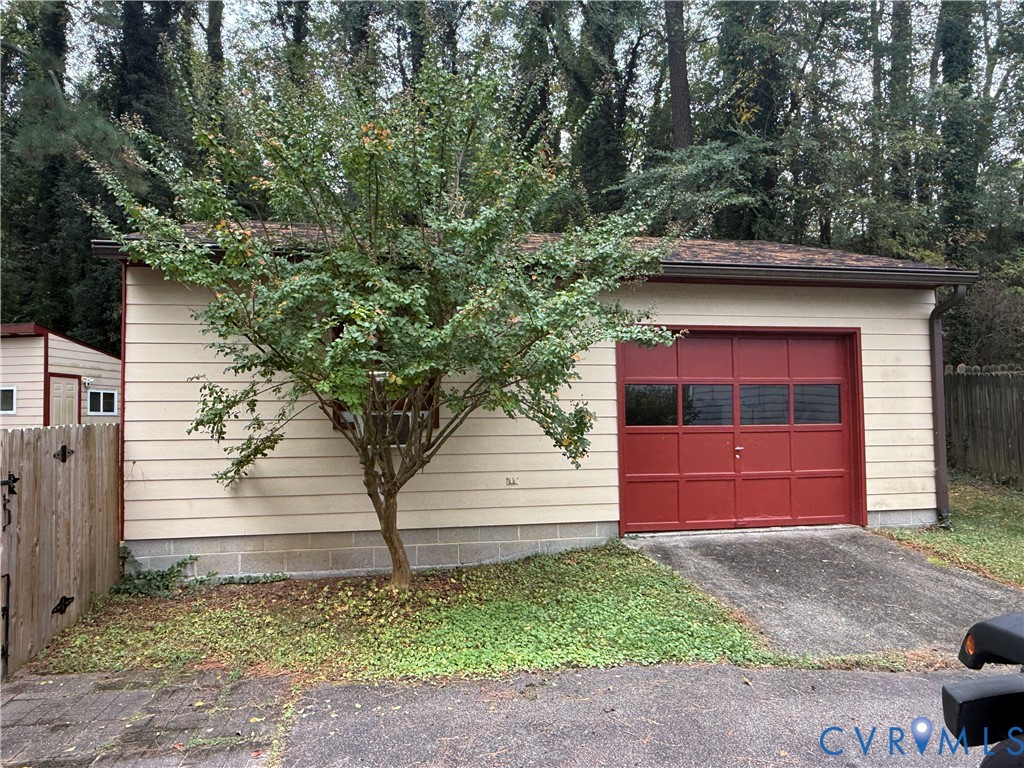 Detached garage featuring light-colored horizontal siding, a red sectional garage door with window panels, and a concrete driveway apron Detached garage featuring light-colored horizontal siding, a red sectional garage door with window panels, and a concrete driveway apron