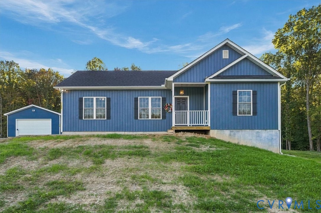 Expansive open grounds featuring a blue-sided outbuilding, a gravel driveway, and a border of mature trees