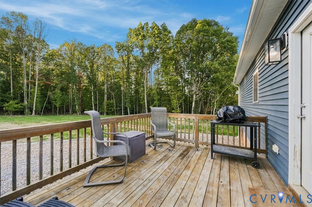 Blue siding exterior featuring a raised wood deck, stone-filled landscaping, and concrete hardscaping