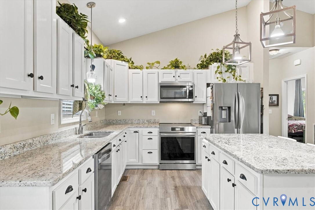 Vaulted ceiling with a central multi-blade ceiling fan, wood-finish flooring, and an island featuring a countertop with integrated seating