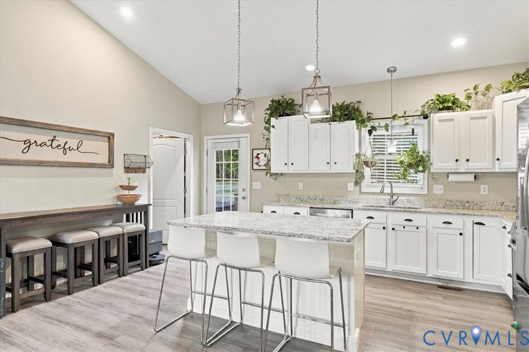 Kitchen featuring white cabinetry, stone-surface countertops, center island with seating, vaulted ceiling, and wood-finish flooring Kitchen featuring white cabinetry, stone-surface countertops, center island with seating, vaulted ceiling, and wood-finish flooring
