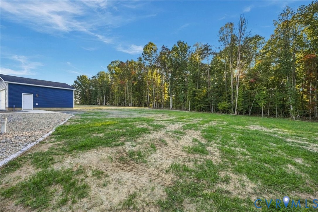 Single-story residence featuring a gray exterior, a detached garage, and a gravel driveway situated on a cleared lot with mature trees