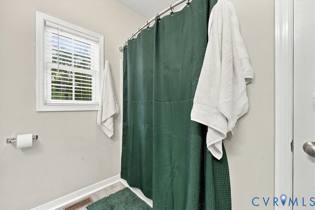 Bathroom featuring a double-hung window with white faux-wood blinds and a metal tension shower rod